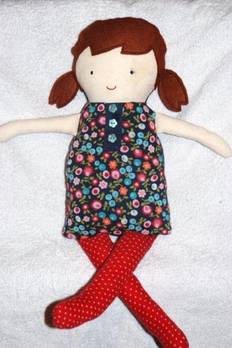 black apple doll with brown hair with pigtails, a floral dress, and red tights
